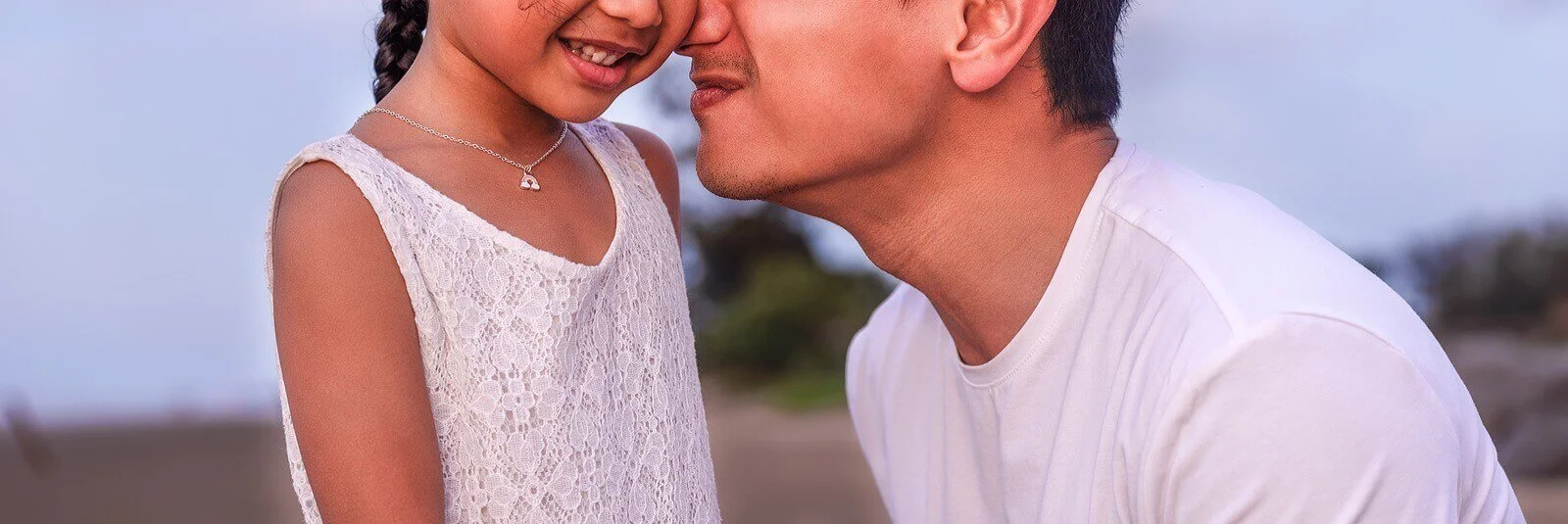 Father and young daughter smiling and touching noses outdoors, representing a warm parent-child relationship