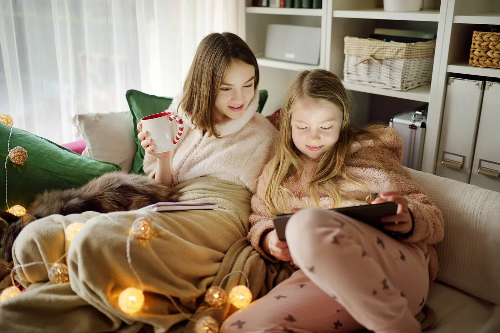 Two children relaxing at home during winter break while reading and using a tablet together