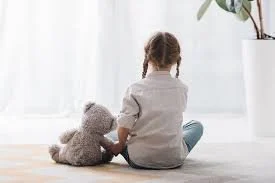 How children react to grief and loss shown by child sitting quietly with stuffed animal in a reflective moment