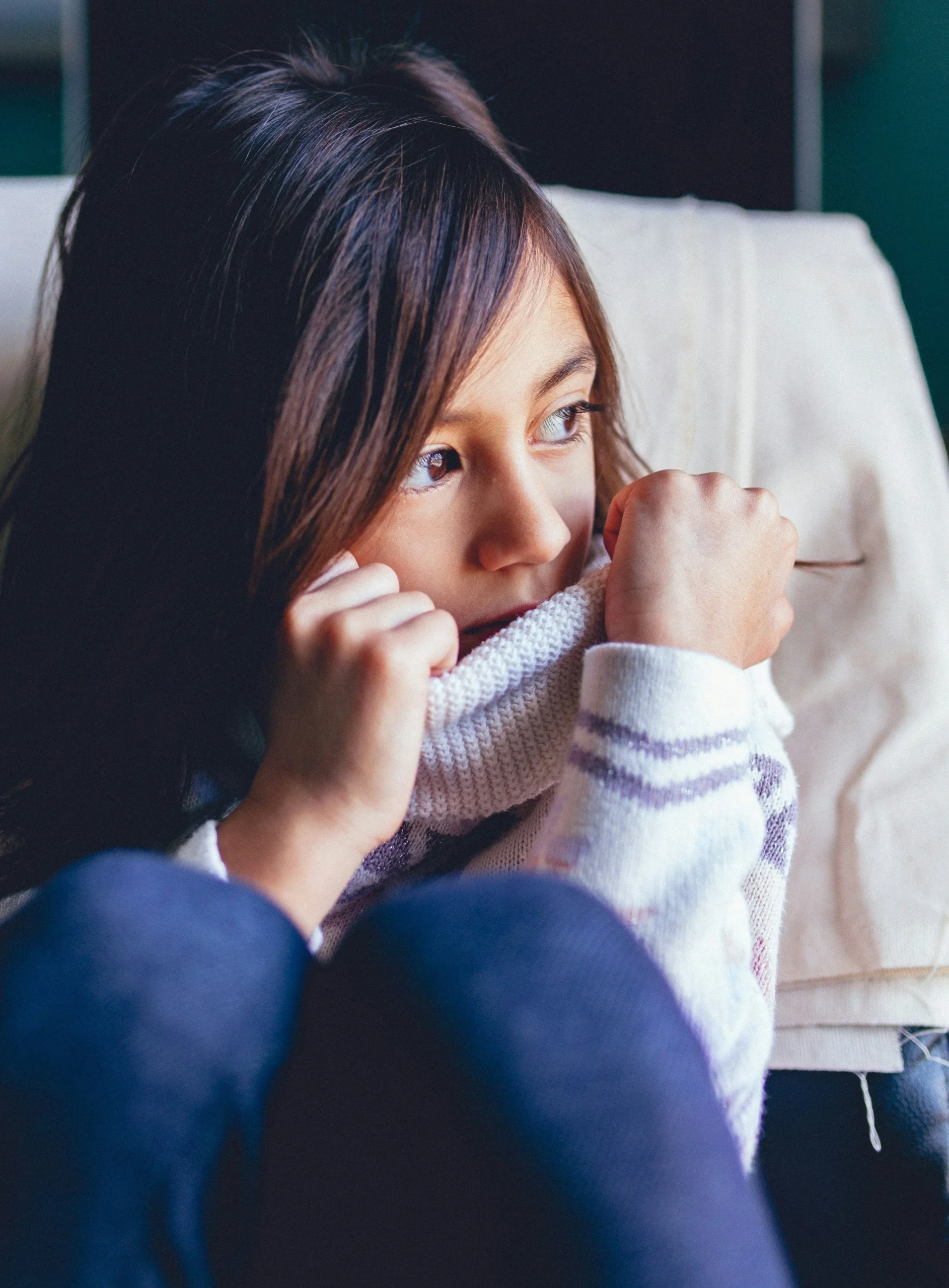 Signs of grief in a child shown by young girl sitting alone indoors looking worried and withdrawn