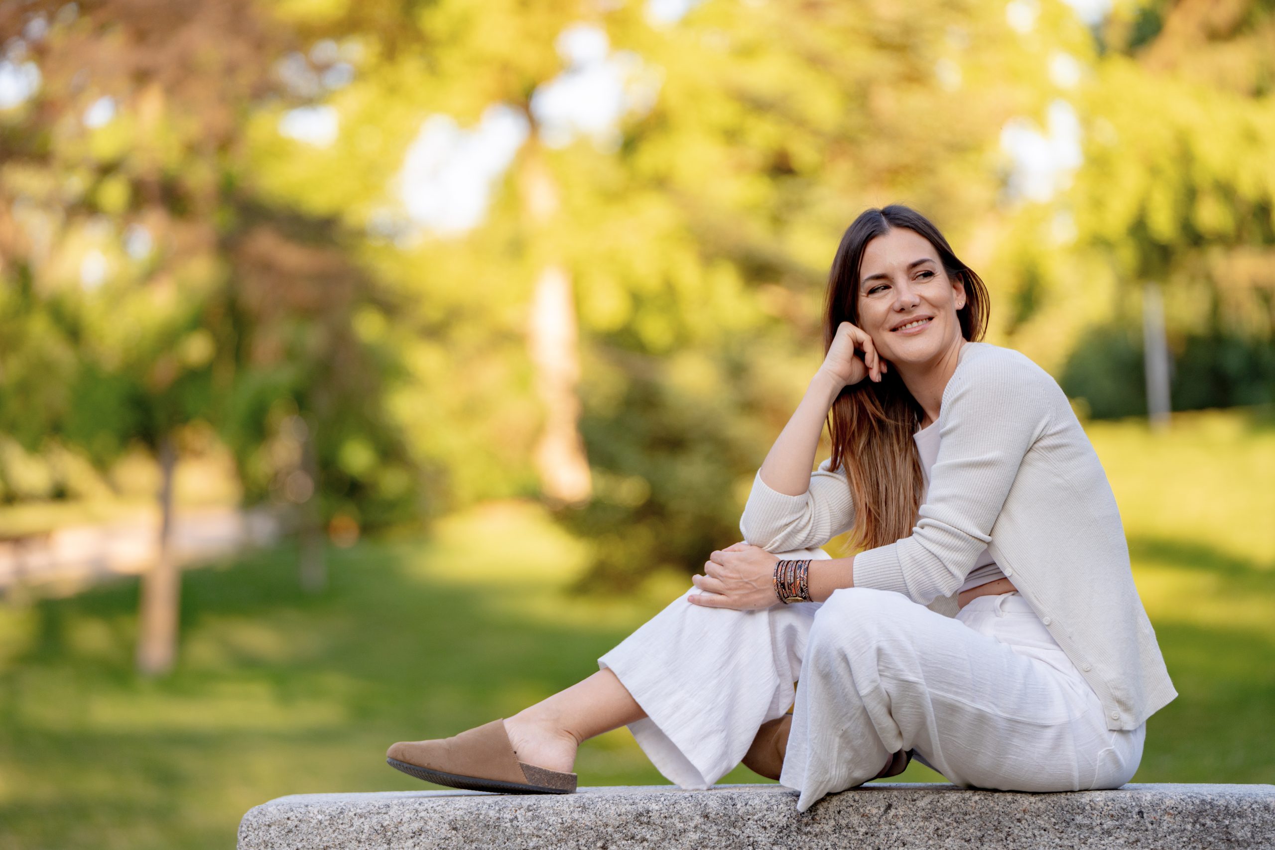 A woman on a park bench, smiling happily, surrounded by nature on a sunny day, enjoying the peaceful atmosphere