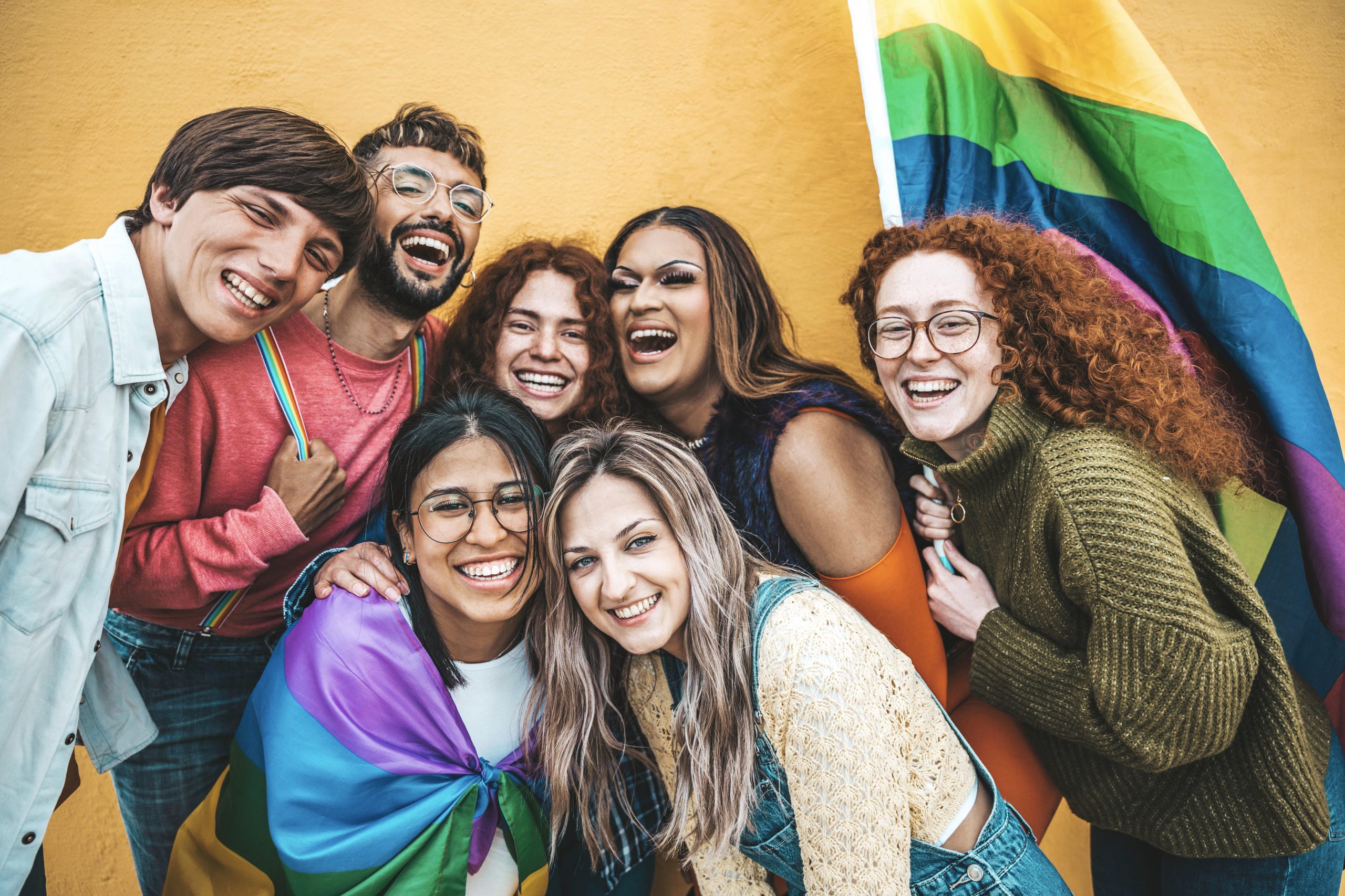 Diverse group of young people celebrating gay pride festival day - Lgbt community concept with guys and girls hugging together outdoors - Multiracial trendy friends standing on a yellow background