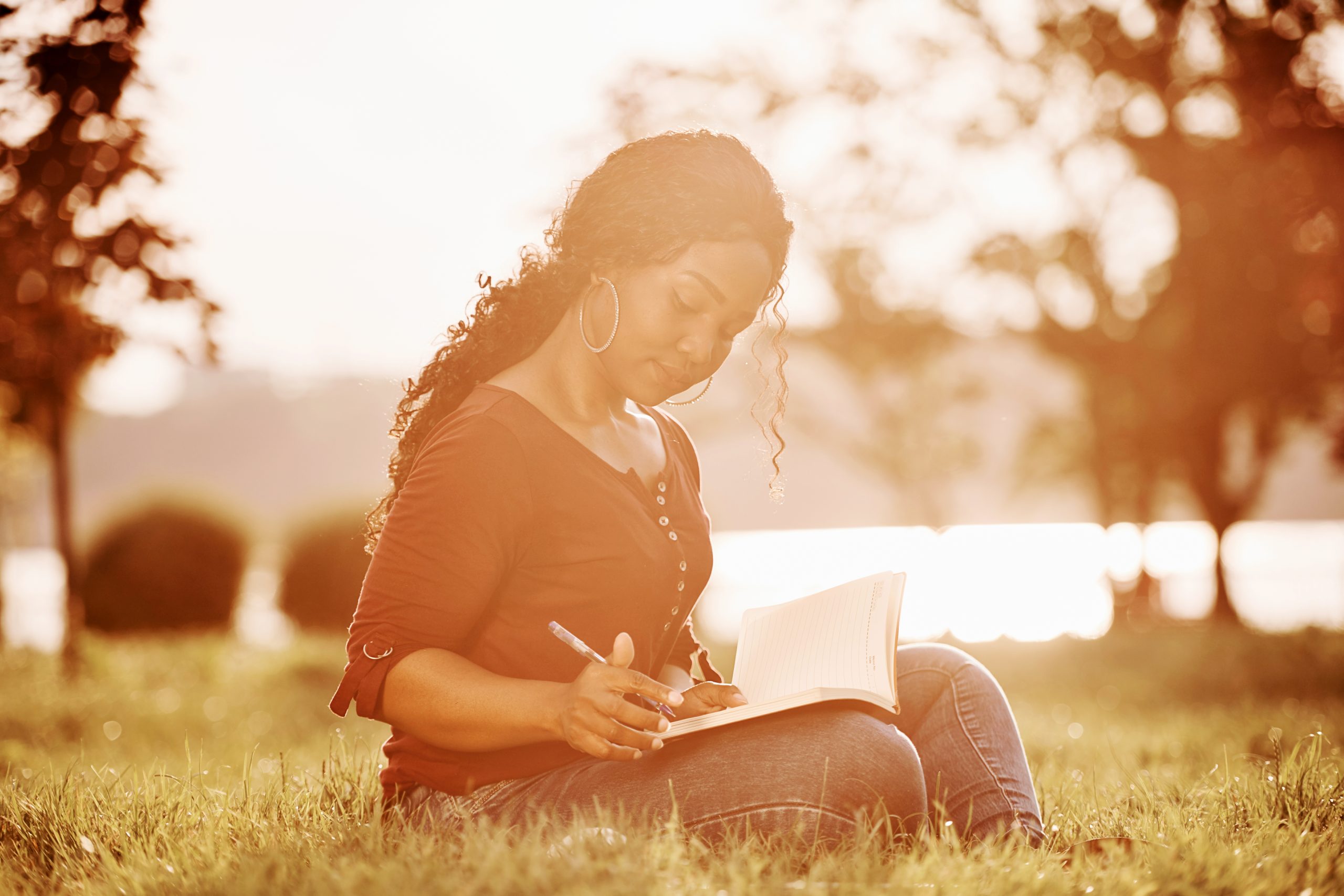 Woman sitting on the grass journaling in warm golden sunlight.