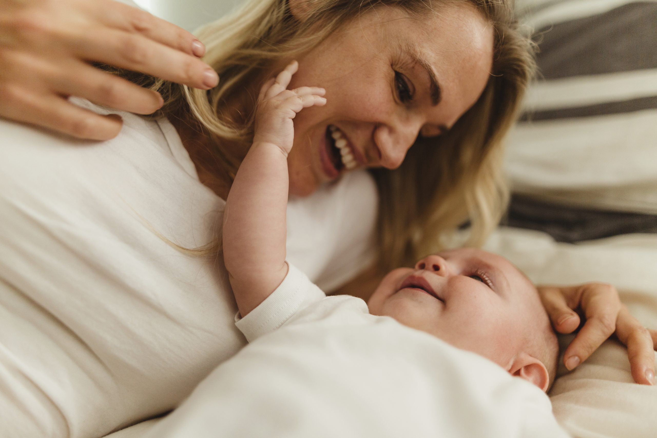 Mother lying beside her baby, smiling and playing together.