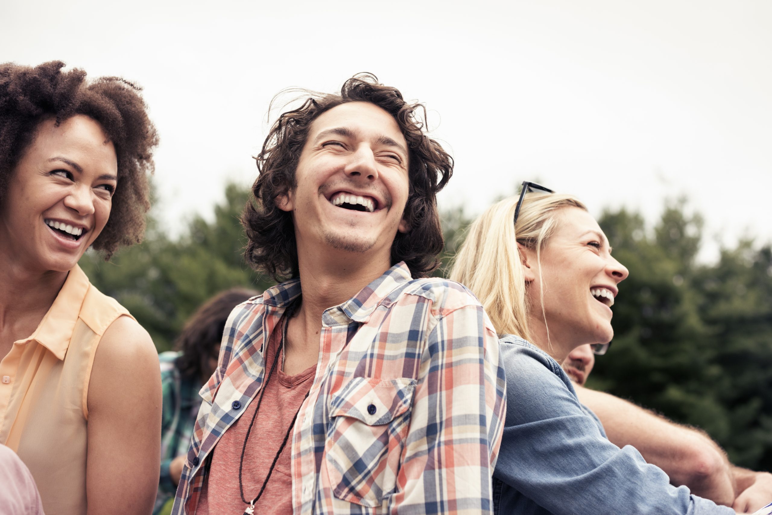 Young adults laughing together outdoors at a gathering.