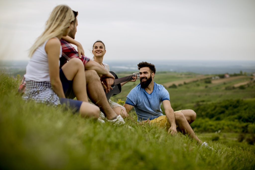 Group of young people sitting on grass and having fun on a field trip in nature on a mountain