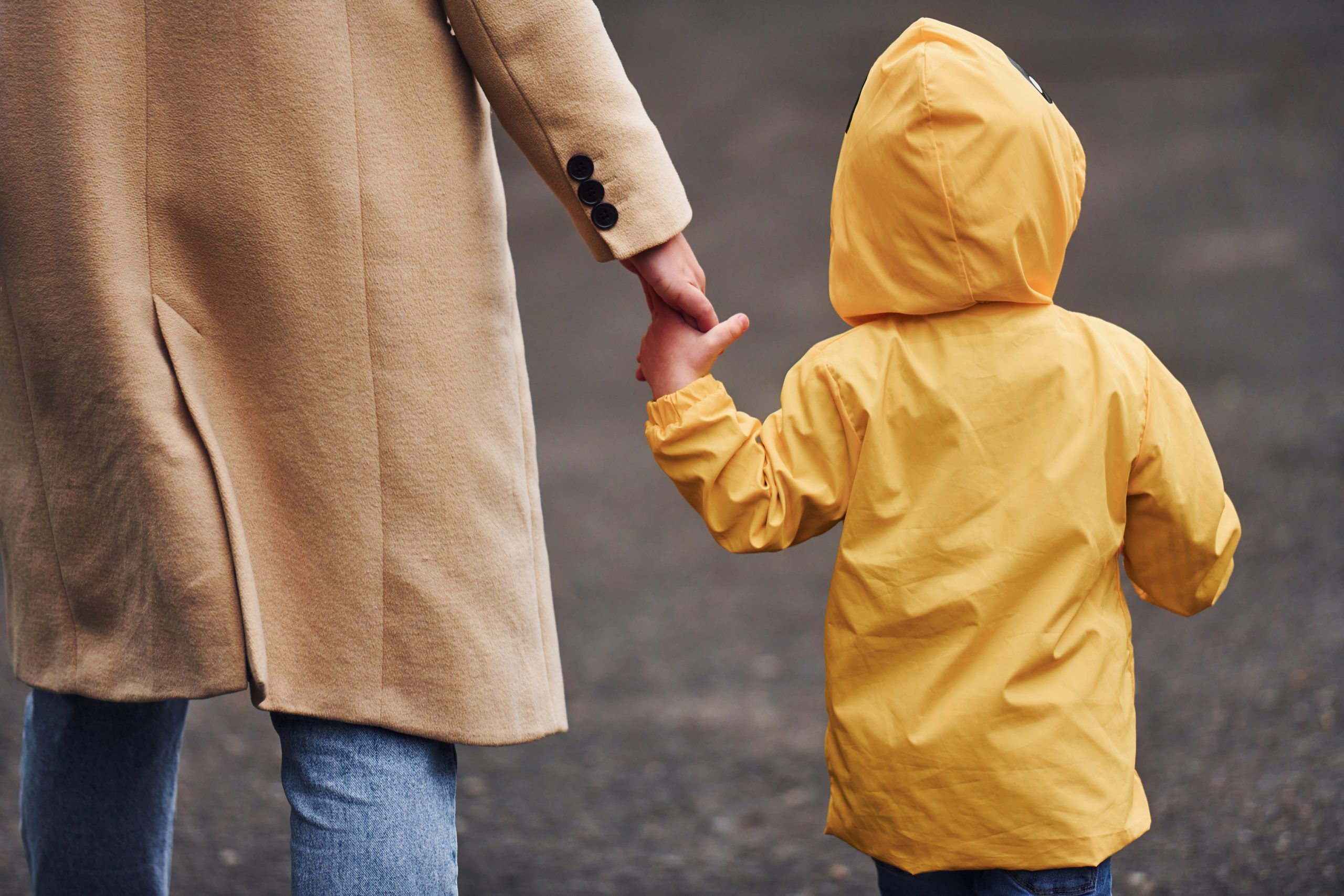 Adult holding hands with a child in a yellow raincoat while they walk.