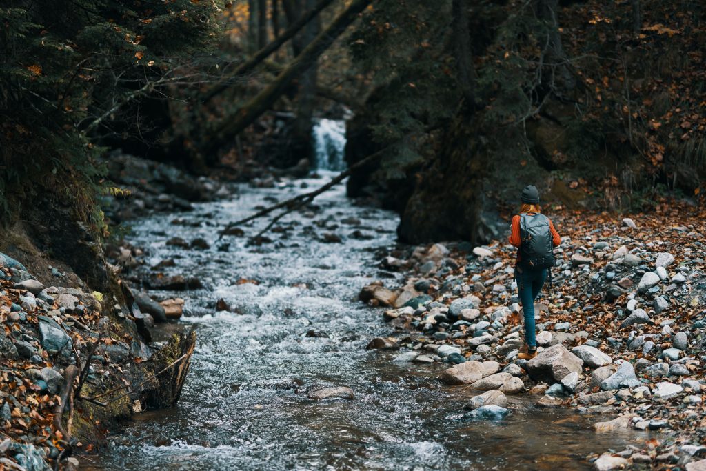 Hiker walking along a rocky stream with a small waterfall in the distance.