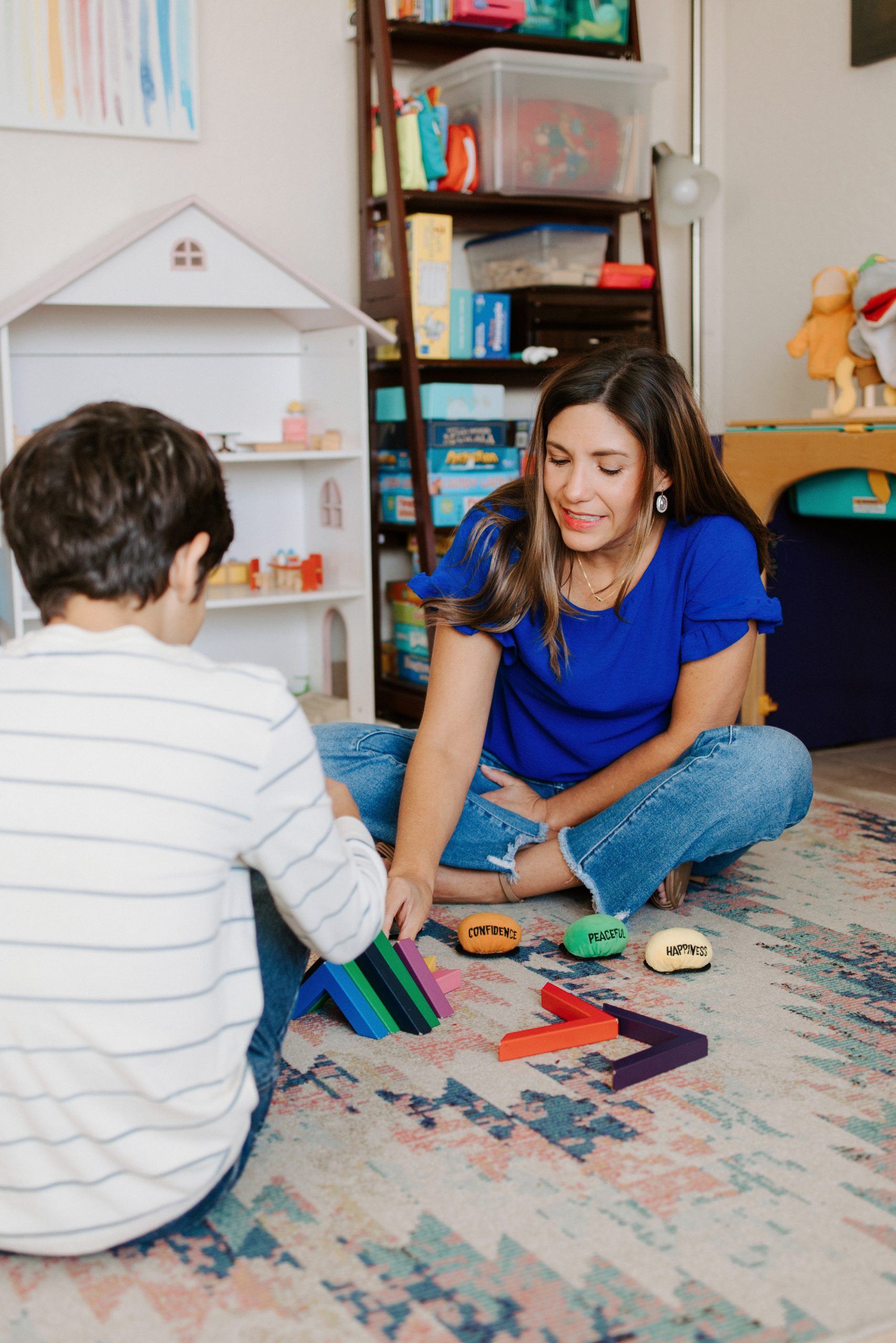 Therapist sitting on the floor playing with children and toys in a bright room.