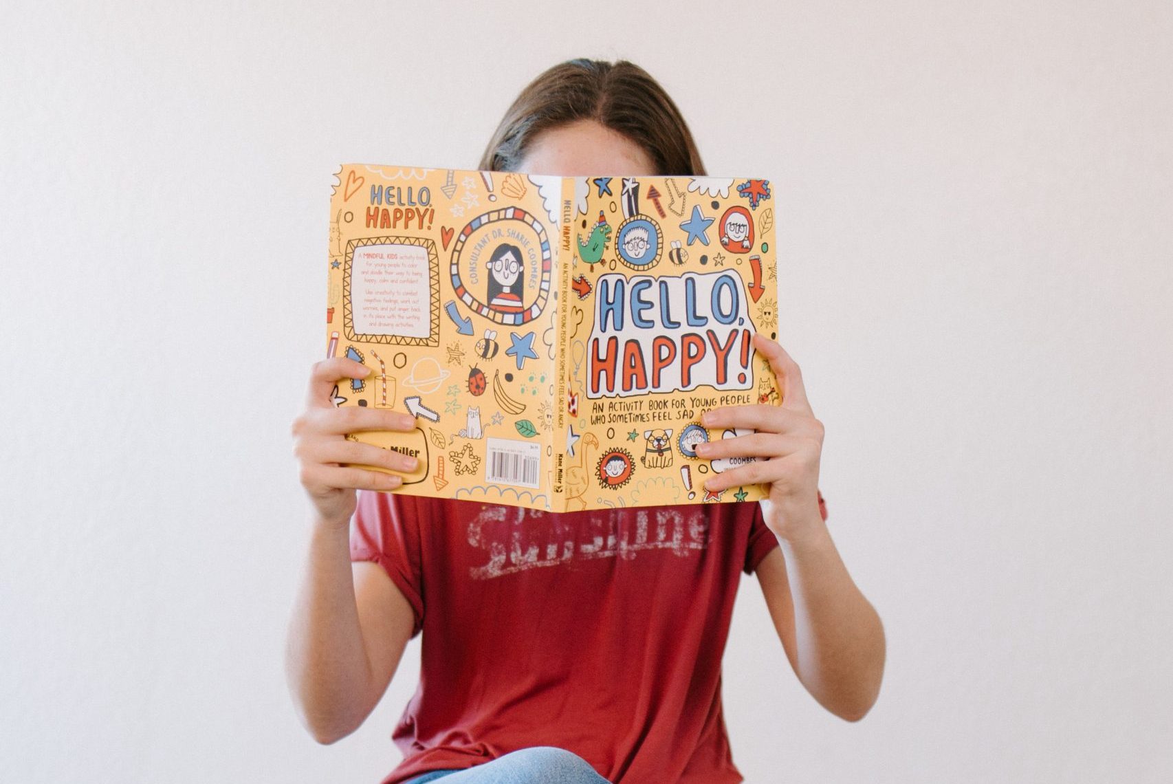 Child holding a bright “Hello Happy” book in front of their face.