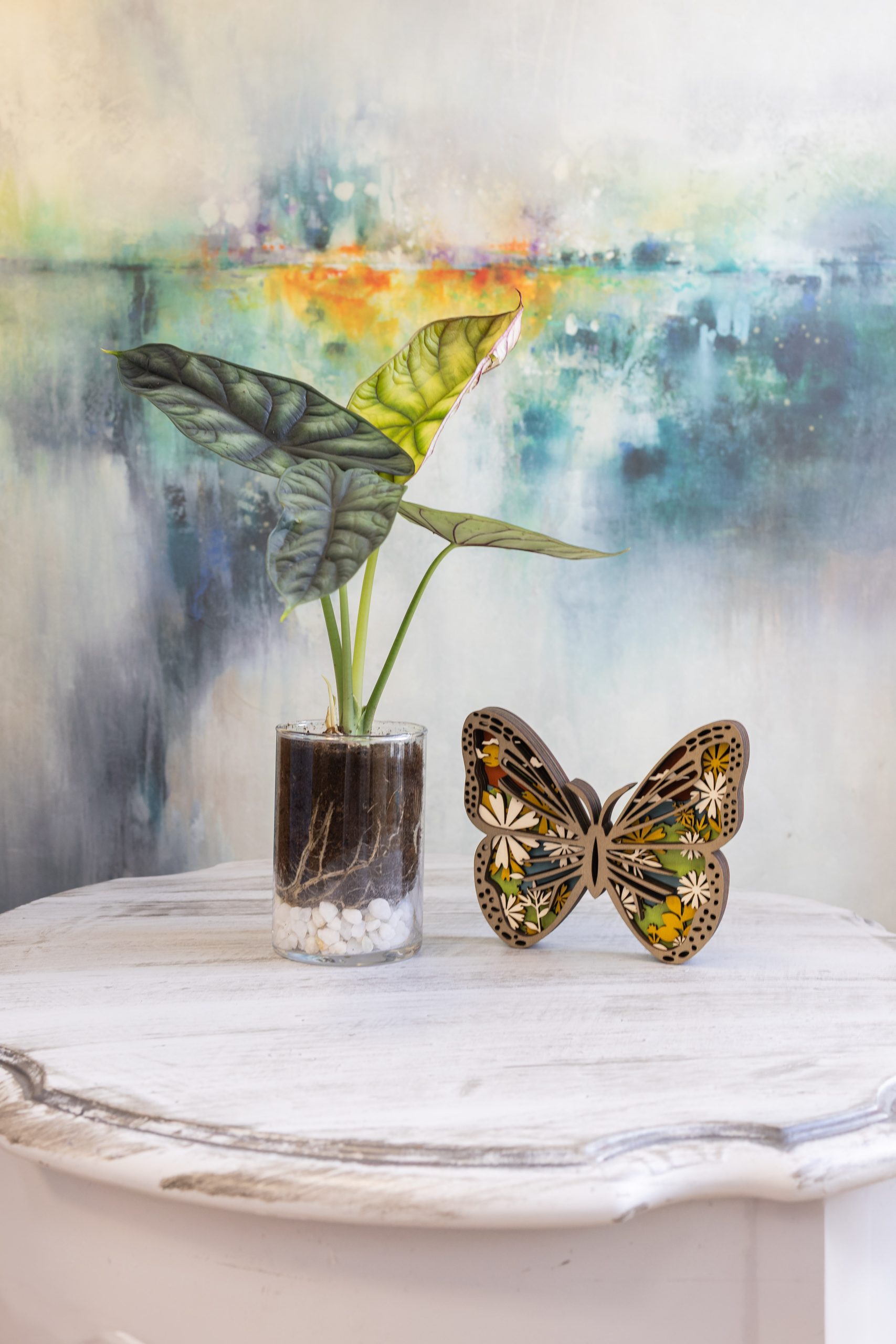 Decorative vase and butterfly art displayed against a colorful painted background.