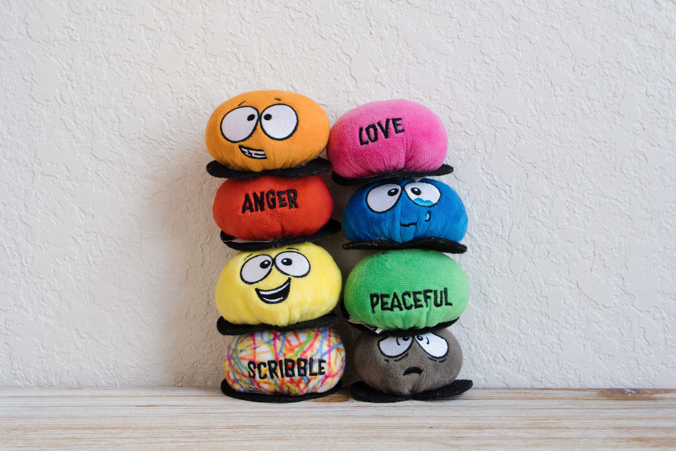 Stack of colorful plush emotion faces labeled anger, love, peaceful, and other feelings.