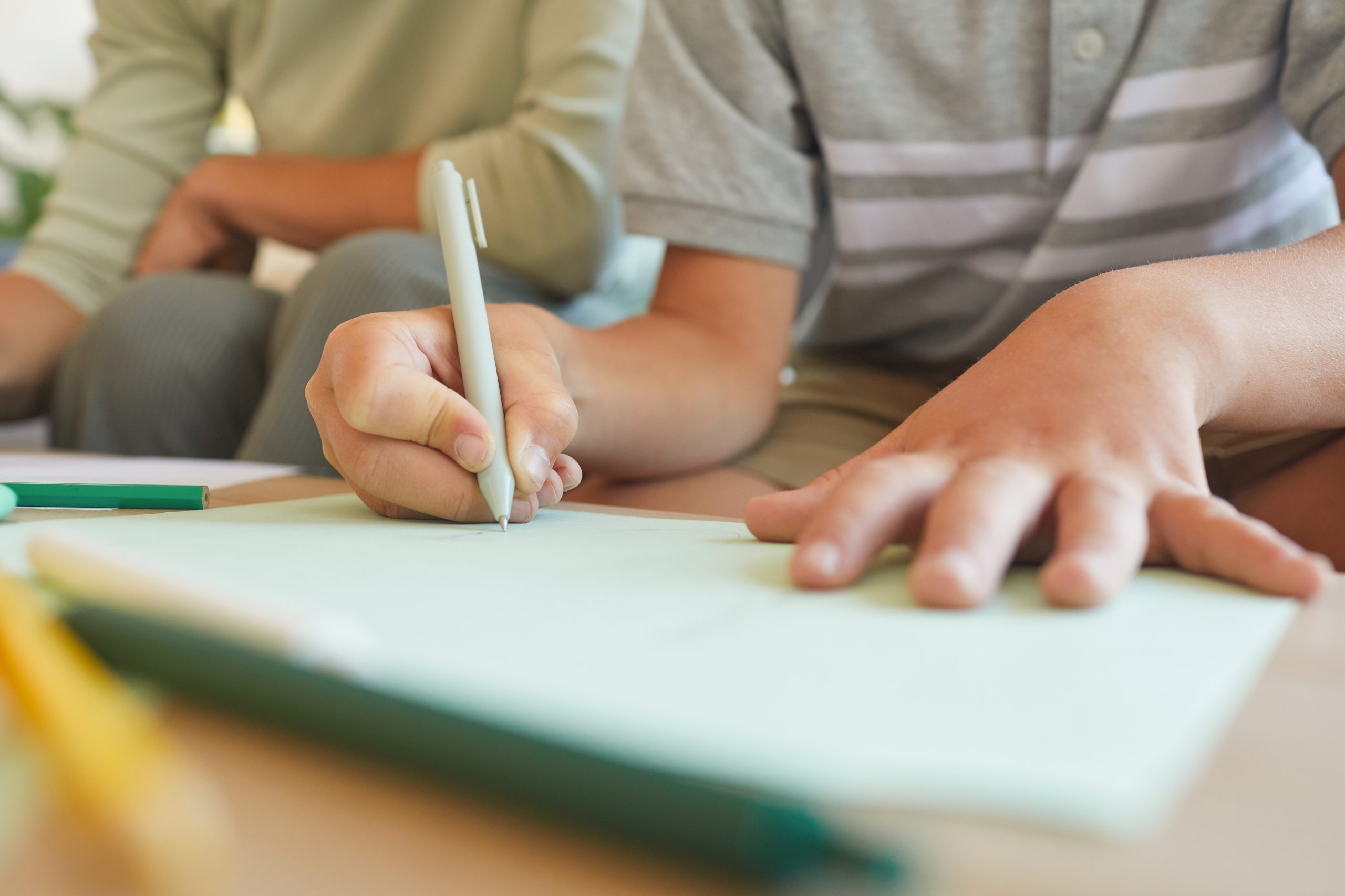 Child’s hand writing on a teal clipboard or workbook.