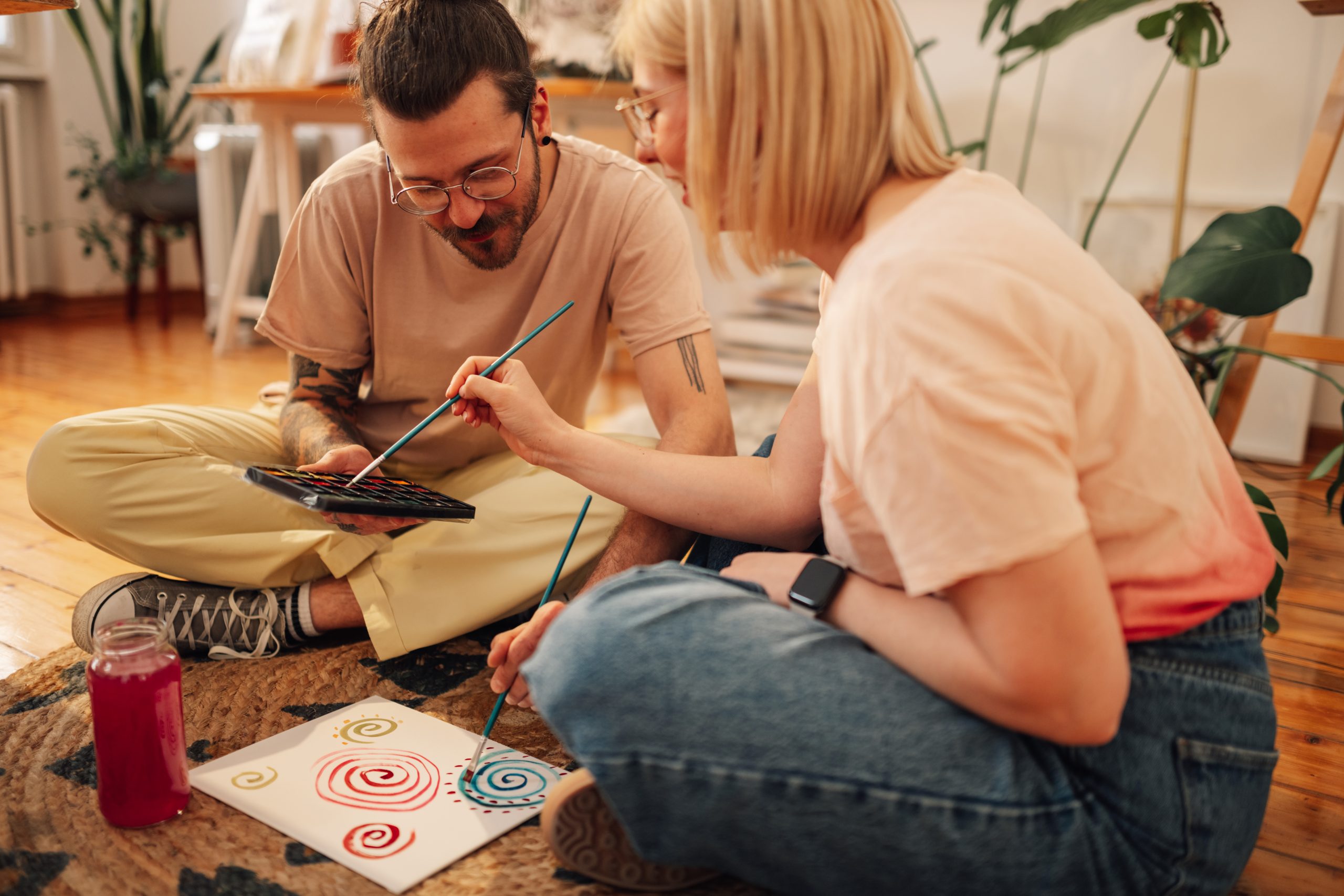 Two adults sitting on the floor painting colorful spiral designs together.