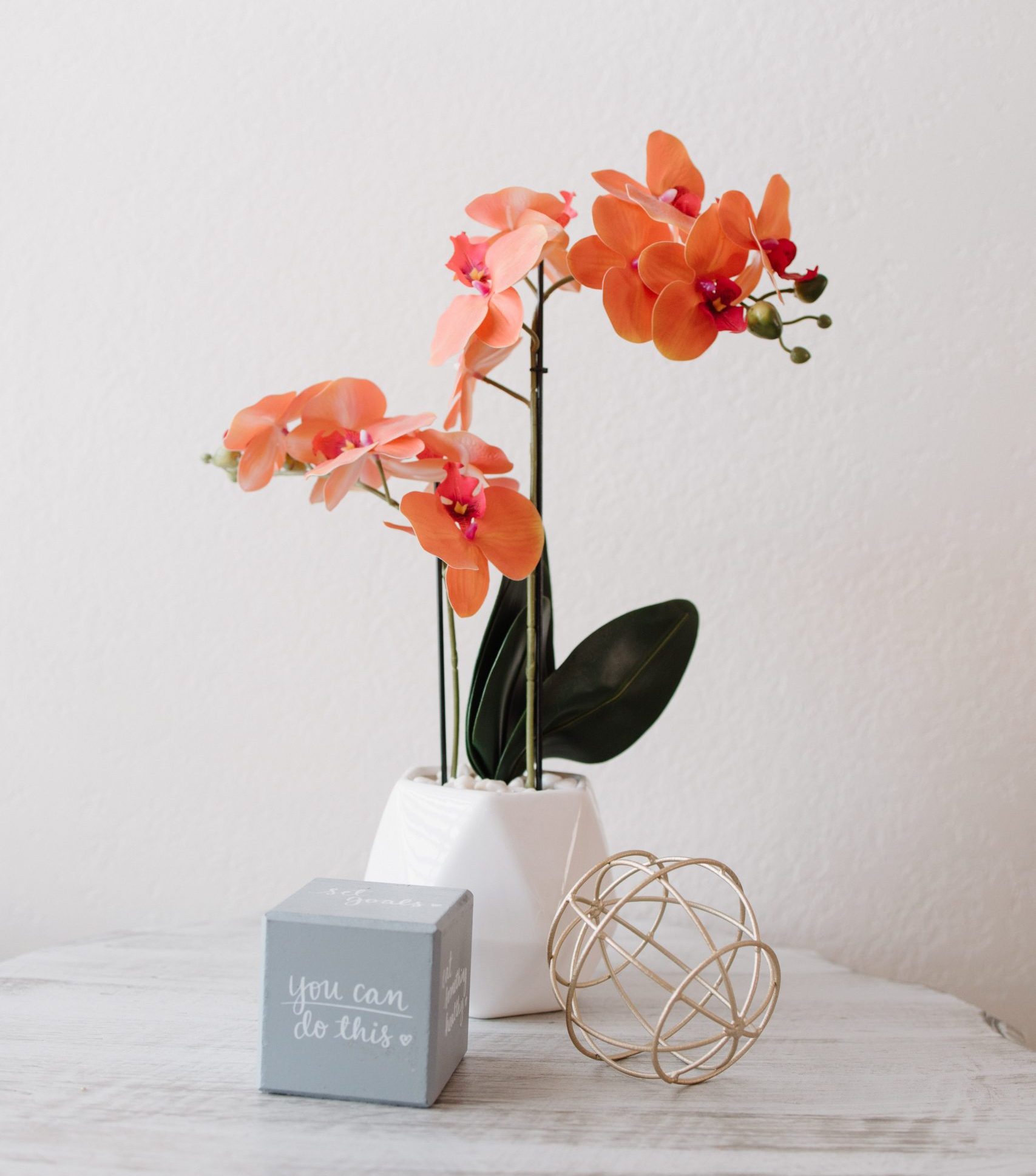 Orange orchid in a white vase on a light tabletop.